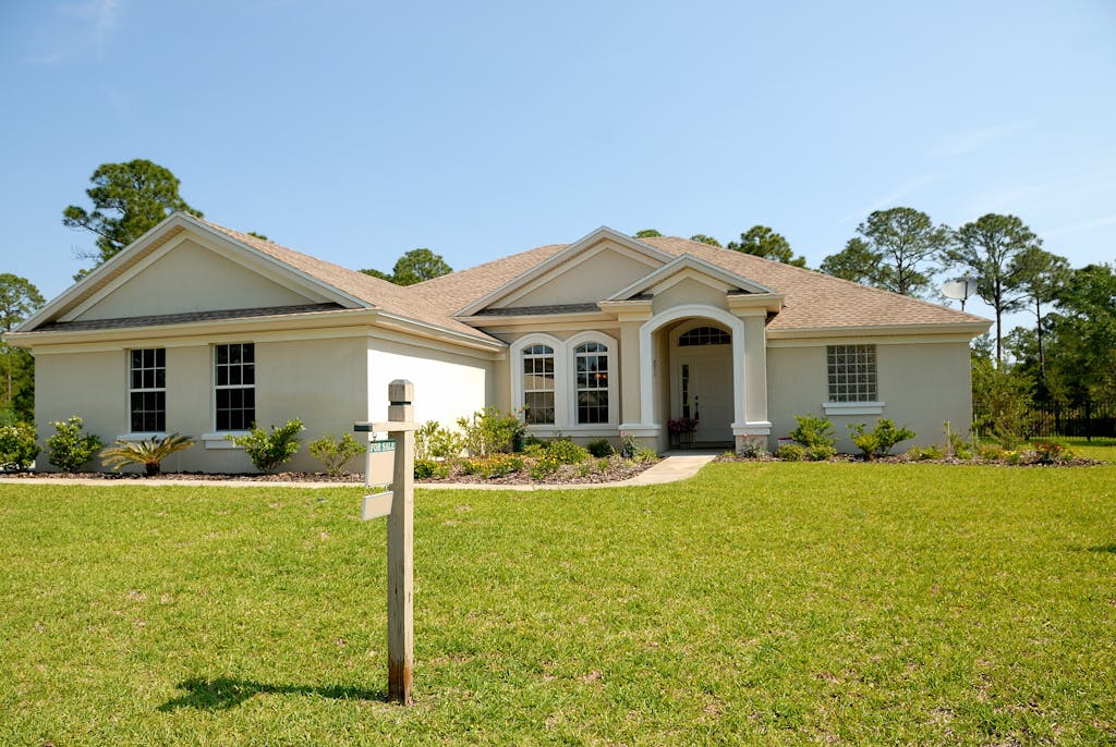 Beautiful suburban house with lush lawn, showcasing a for sale sign under a clear blue sky.